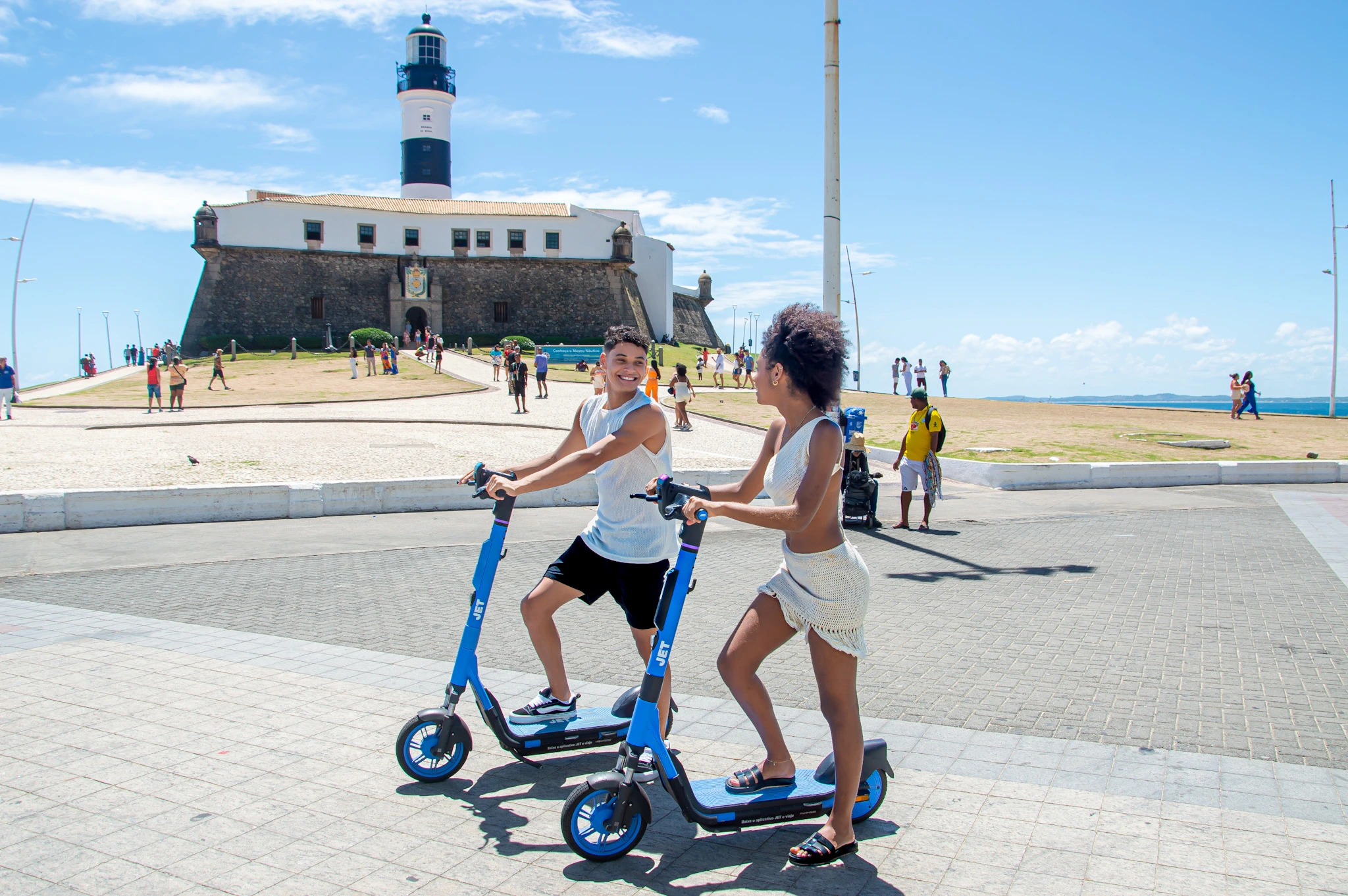 Two friends on JET e-scooters by the Farol da Barra lighthouse in Salvador